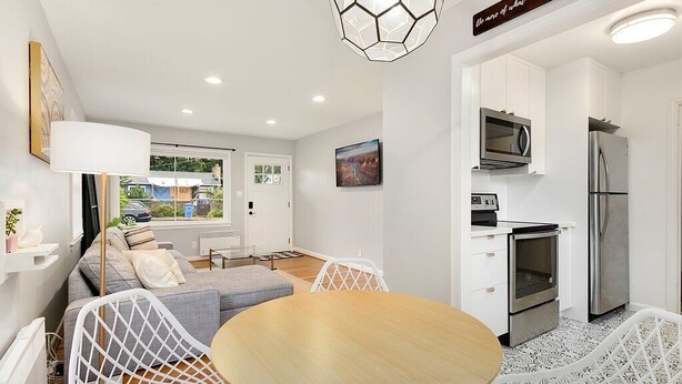 A modern kitchen with white cabinets, stainless steel appliances, and a dining area with a round table and white chairs.