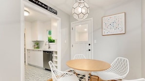 A dining area with a round table and white chairs, a kitchen in the background, and a door with a 'HAPPY' sign.