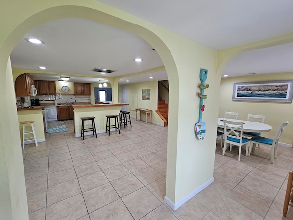 A spacious kitchen with a central island, a dining area with a white table and chairs, and a hallway leading to a staircase.