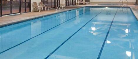 An indoor swimming pool with clear lane markings, adjacent lounge chairs, and a modern ceiling design.
