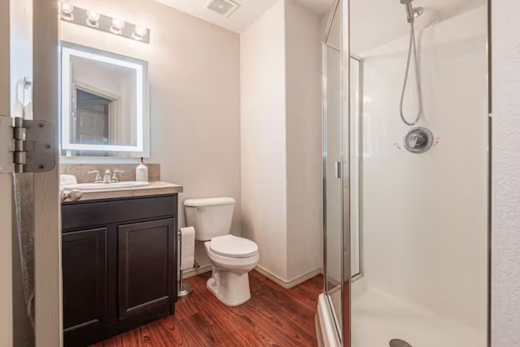 Een moderne badkamer met een douchecabine van glas, een donker houten wastafelmeubel en een wit toilet.