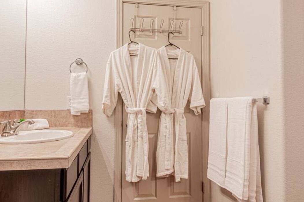 A bathroom with a sink, two white robes hanging on a rack, and a towel rack with a towel.