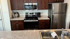 A kitchen with dark wooden cabinets, stainless steel appliances including a microwave, oven, and refrigerator, and a granite countertop. - Downtown Memphis Loft! Walking distance from Beale street! Garage parking! (Memphis)