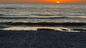 A beach scene with the sun setting over the ocean, waves crashing onto the shore, and a clear sky. - May availability: Waterfront corner unit, private patio, first floor (Indian Shores)