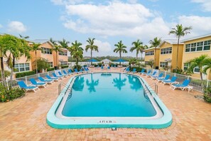 A swimming pool with lounge chairs and palm trees, surrounded by buildings.