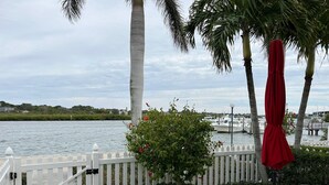 A waterfront patio with a white fence, a table with chairs, and a red umbrella. - May availability: Waterfront corner unit, private patio, first floor (Indian Shores)