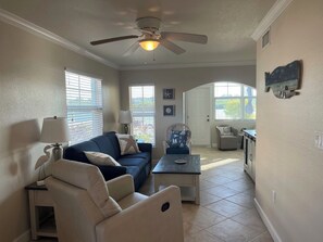 A living room with a ceiling fan, a sofa, a coffee table, and a dining area with a chair. - November/December availability: Waterfront corner unit, private patio, 1st floor (Indian Shores)