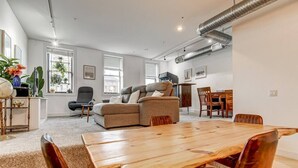 Ein modernes Wohnzimmer mit einem Holzesstisch, einem grauen Sofa und einem kleinen Beistelltisch mit Globus und Pflanzen.