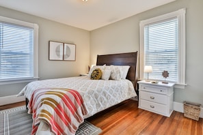 A bedroom with a bed, nightstands, a lamp, and a window with blinds.