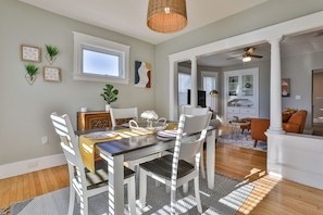 A dining area with a table set for four, surrounded by white chairs. There is a window above the table, and a ceiling fan above the dining area.