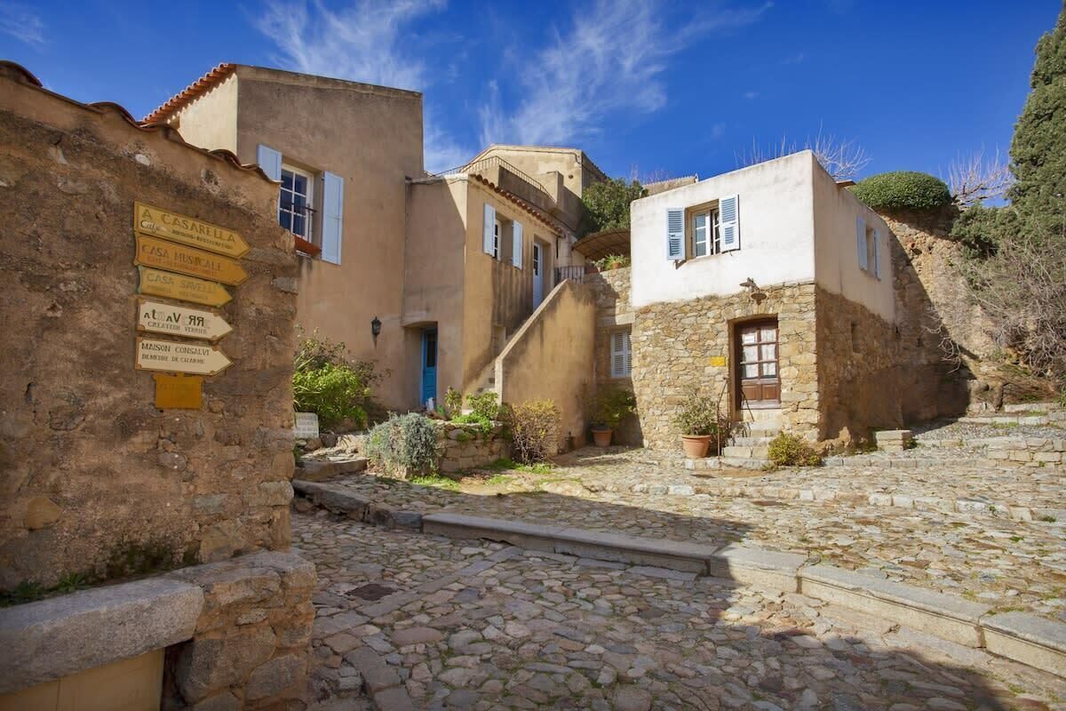 A stone-paved courtyard with traditional buildings, a staircase, and a signpost with directions.
