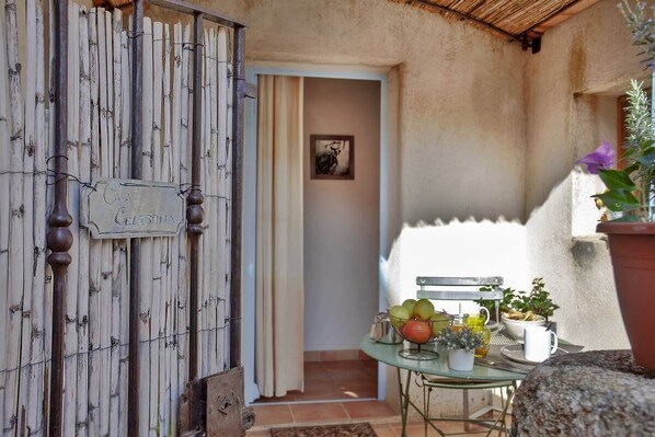 A rustic outdoor area with a wooden gate labeled "Casa Cezetina," a glass table with a bowl of fruit and a potted plant, and a doorway leading to an interior space. - Casa Celestina – Chambre indépendante de charme au cœur de Pigna (Pigna)