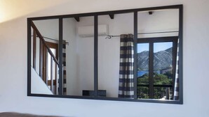 Quarto com um espelho grande refletindo uma escada, uma janela com vista para montanhas e uma cortina listrada.