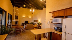 A compact kitchen with wooden cabinets, a microwave, and a toaster. There is a dining area with a table and chairs, and a sofa in the background. - Casa Cholotío lake view, modern, beach access (Panajachel)