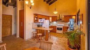 A spacious kitchen with wooden cabinets, a central island with stools, a large water dispenser, and a potted plant. - Casa Cholotío lake view, modern, beach access (Panajachel)