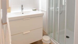 A modern bathroom with a white vanity, a round mirror, a glass shower enclosure, and a wooden floor. - Apartment Le Cocooning (Tours)