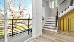 Een modern interieur met een trap, een balkon met metalen hekwerk en uitzicht op bomen en gebouwen.