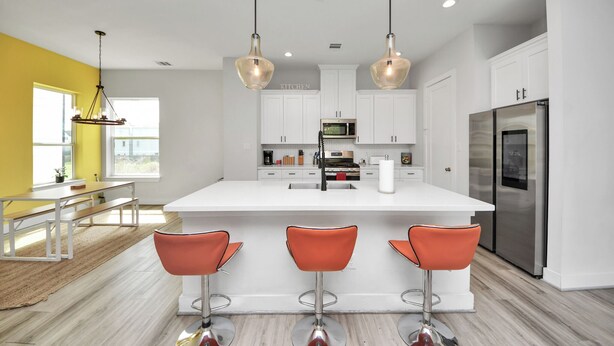 Een moderne keuken met een centraal eiland, barkrukken en roestvrijstalen apparatuur.