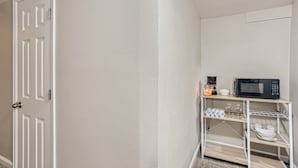 Une pièce avec une porte blanche, un mur blanc et une étagère blanche contenant un four à micro-ondes, des tasses et des verres.