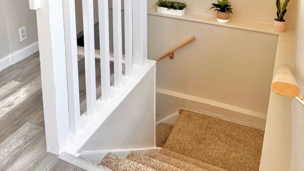 Un escalier avec une rampe blanche, une petite étagère avec des plantes et un luminaire fixé au mur.