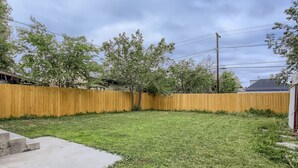 Un jardin avec une clôture en bois, un chemin en béton et une pelouse.