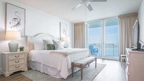 A bedroom with a bed, bedside tables, a bench, a ceiling fan, and a balcony with curtains. - Newly Remodeled 3 Bedroom with Views of Robinson Island and Perdido Bay. Complimentary Boat Slip! (Orange Beach)