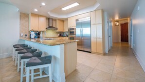 A modern kitchen with a central island, stainless steel appliances, and a hallway leading to a dining area. - Newly Remodeled 3 Bedroom with Views of Robinson Island and Perdido Bay. Complimentary Boat Slip! (Orange Beach)