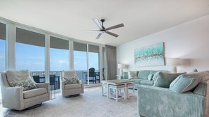 A spacious living room with a large window, a ceiling fan, a green-striped sofa, a white armchair, and a small table. - Newly Remodeled 3 Bedroom with Views of Robinson Island and Perdido Bay. Complimentary Boat Slip! (Orange Beach)