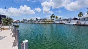 A marina with several waterfront houses, a dock with a boat, and a clear sky. - Waterfront Venture Out Home (Cudjoe Key)