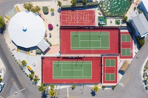 Ein Luftbild eines Sportkomplexes mit mehreren Tennisplätzen, einem Basketballfeld und einer großen, weißen Kuppelkonstruktion.