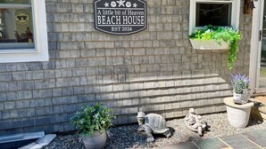 A beach house sign with a rustic brick facade, a small window with a view, and decorative plants and a turtle statue outside.