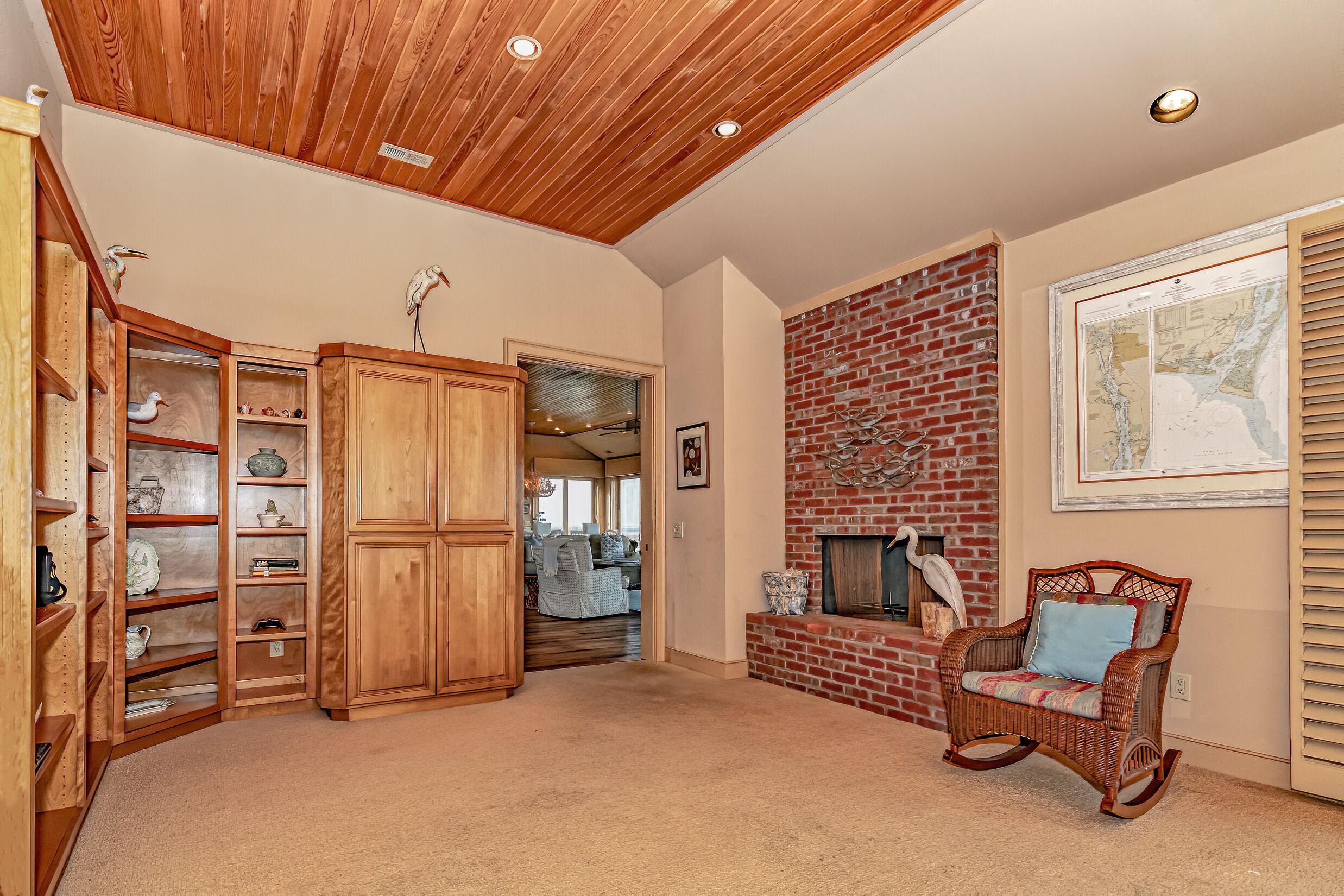 A spacious living room with a wooden ceiling, a brick fireplace, and a wicker rocking chair.