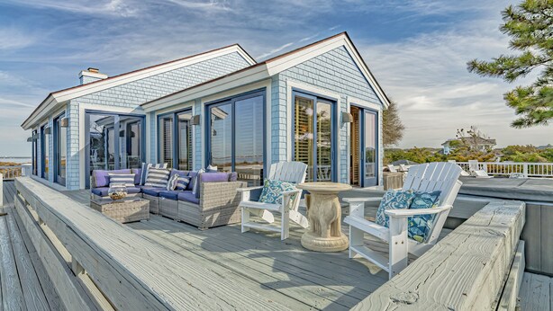 Una casa frente al mar con terraza, amueblada con asientos y una mesa al aire libre.