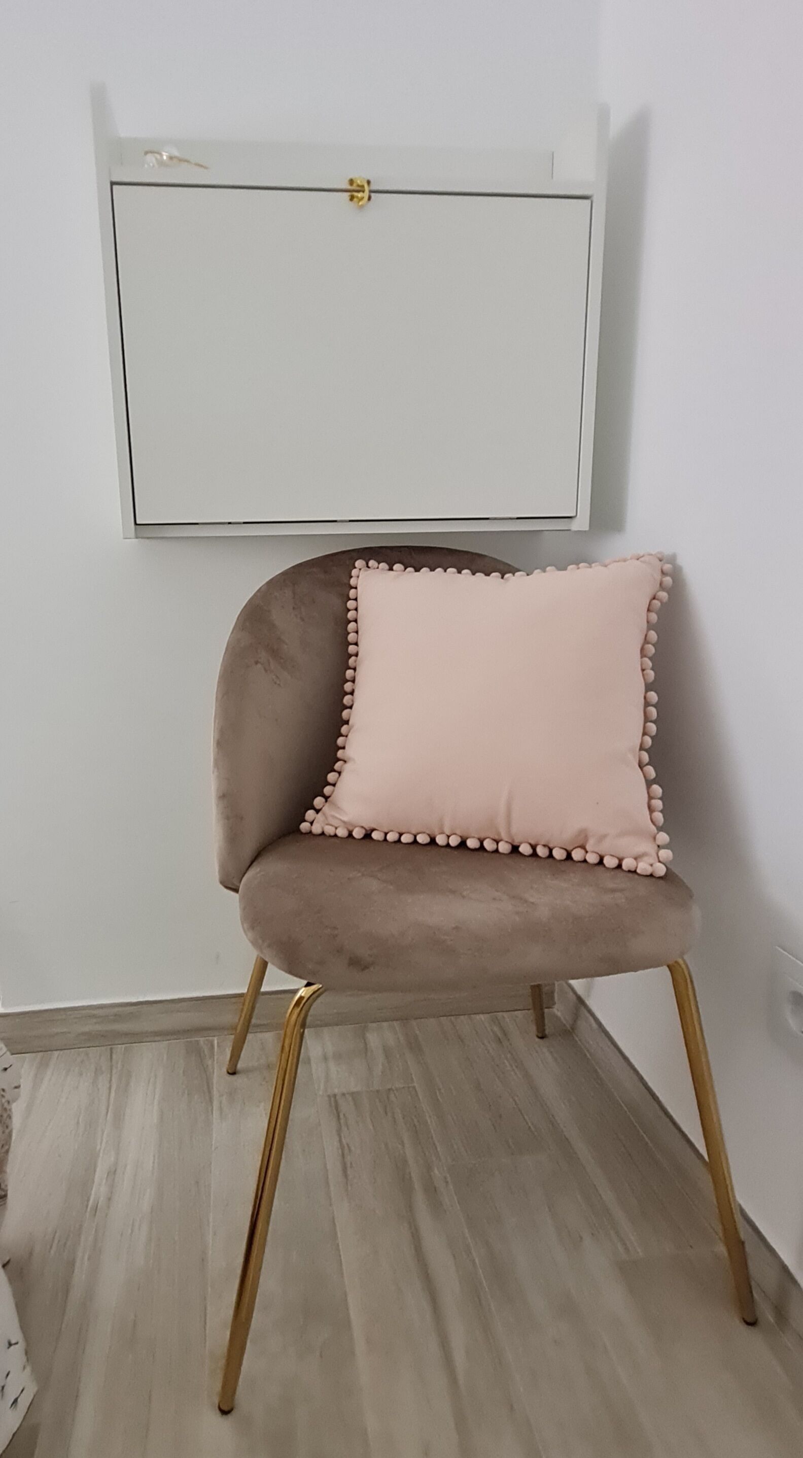 A chair with a plush seat and gold legs, positioned against a white wall with a framed picture above it.