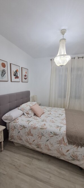 A bedroom with a bed, a nightstand, a chandelier, and three wall-mounted artworks.