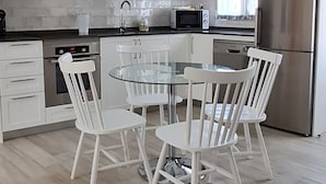 A modern kitchen with white cabinets, a stainless steel refrigerator, a microwave, and a glass dining table with four chairs.