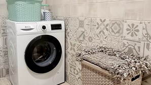A front-loading washing machine next to a wicker laundry basket in a laundry room with patterned tiles.