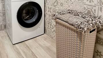 A front-loading washing machine next to a wicker laundry basket in a laundry room with patterned tiles.