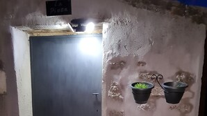 A small, dimly lit room with a dark door, a sign reading "La Pizza," and two hanging planters with green plants.