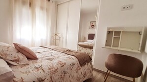 A bedroom with a bed, a chair, a bedside table, and a window with curtains.