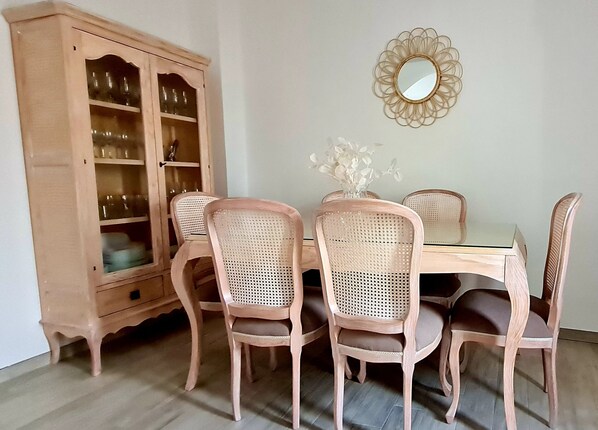 A dining area with a wooden cabinet, four wicker chairs, a glass table, and a wall-mounted mirror.