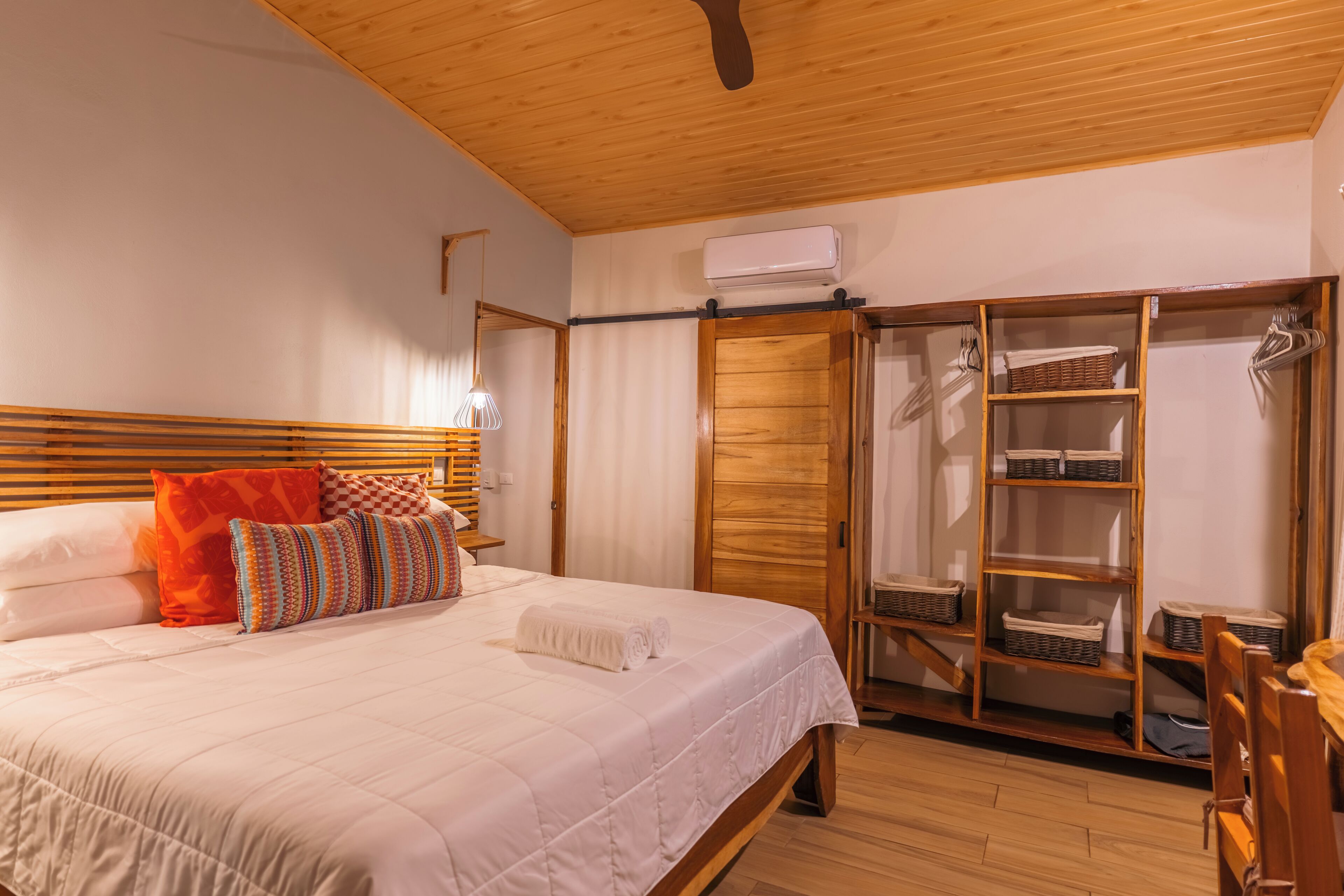 A bedroom with a bed, wooden headboard, a wardrobe with shelves, and a hanging rack.