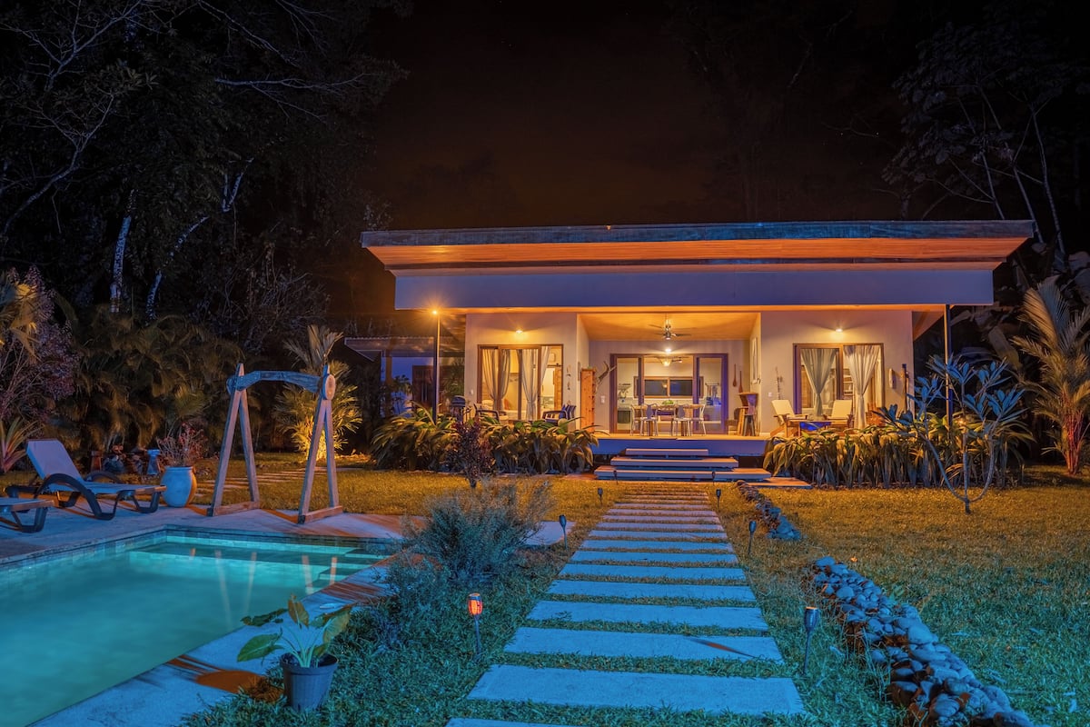 Una casa moderna con piscina, zona de estar exterior e ingreso bien iluminado.