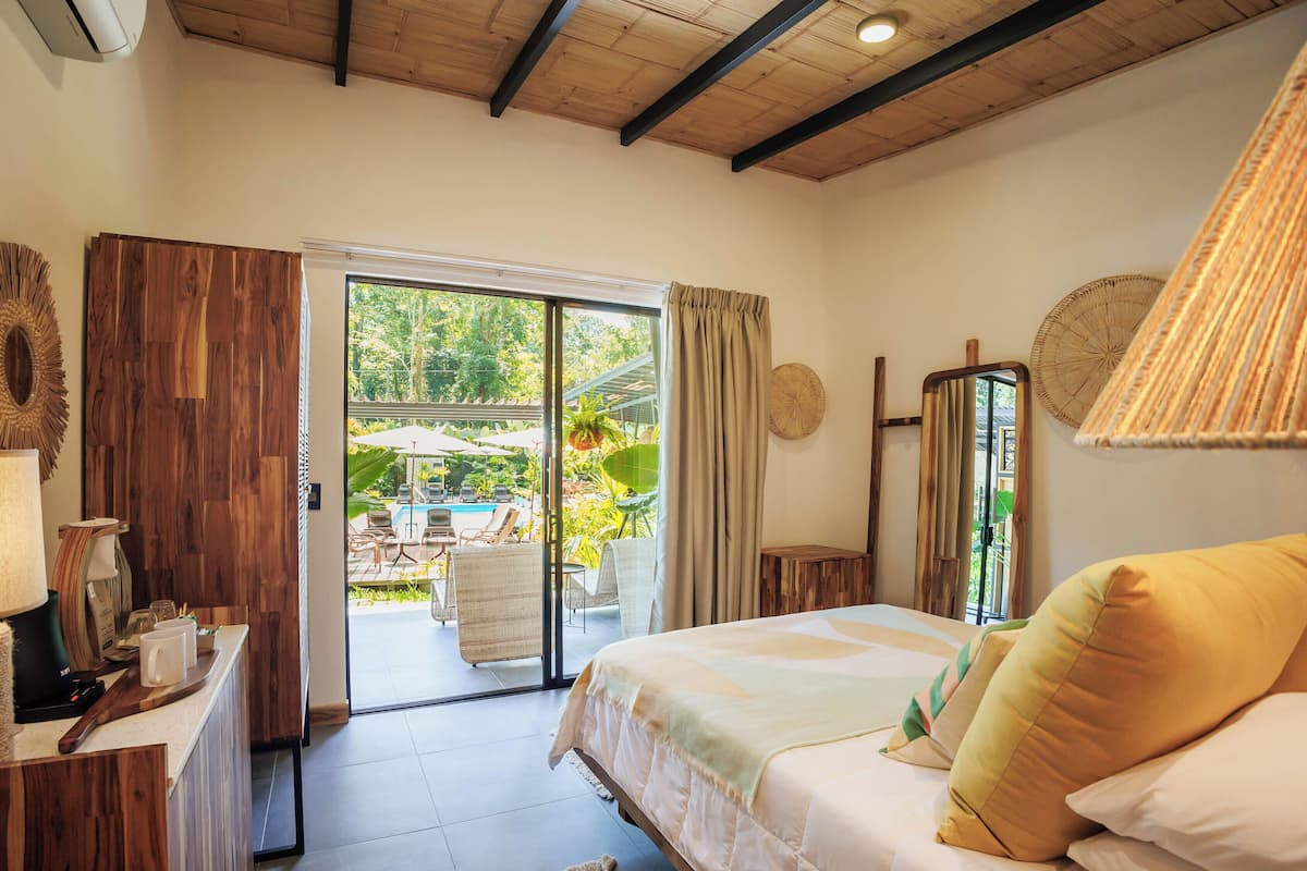 Un dormitorio con cama, escritorio, silla y vistas a un área exterior con piscina y sillas.