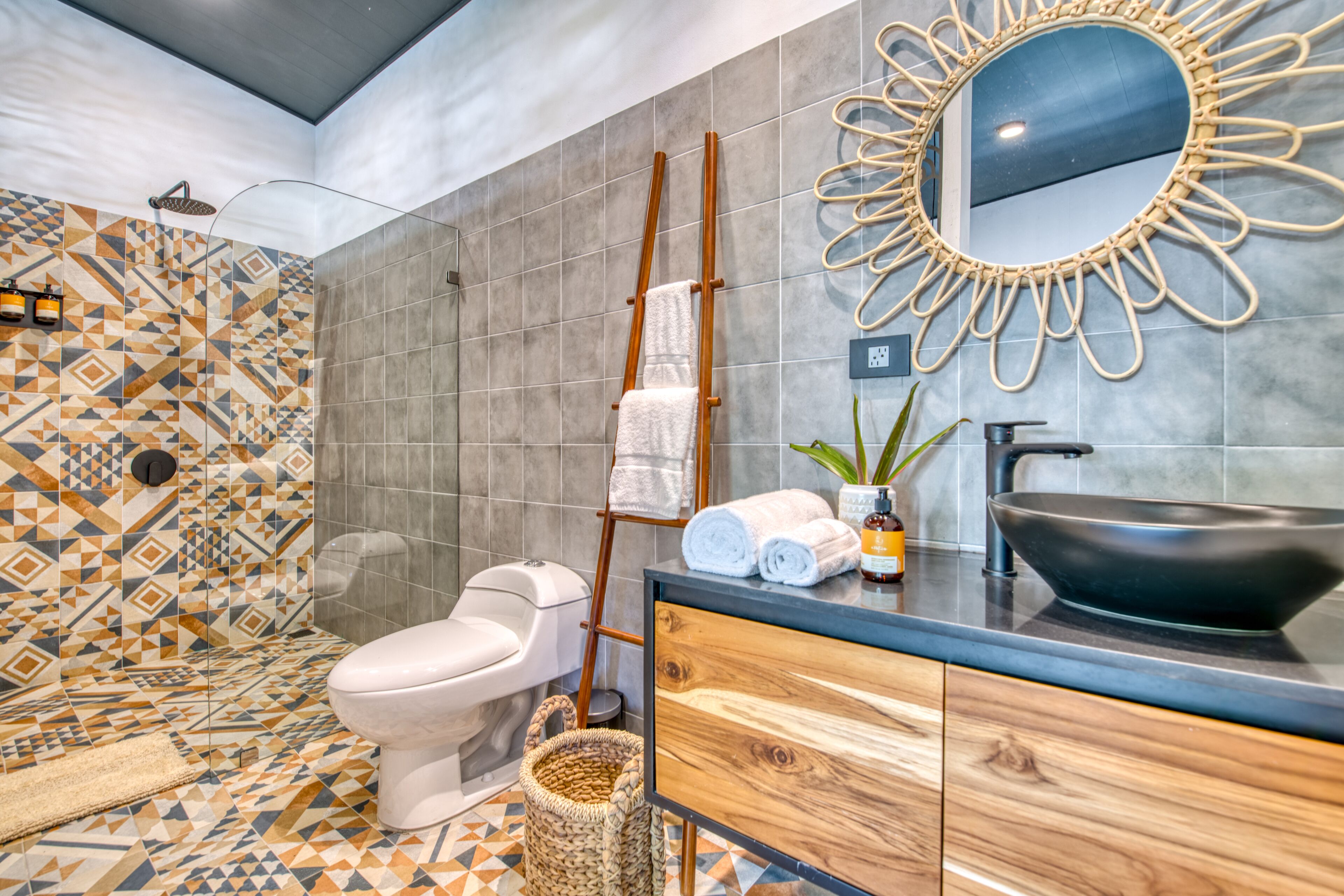Un baño moderno con un salpicadero de azulejos geométricos, un perchero de madera, un lavabo negro y un inodoro blanco.