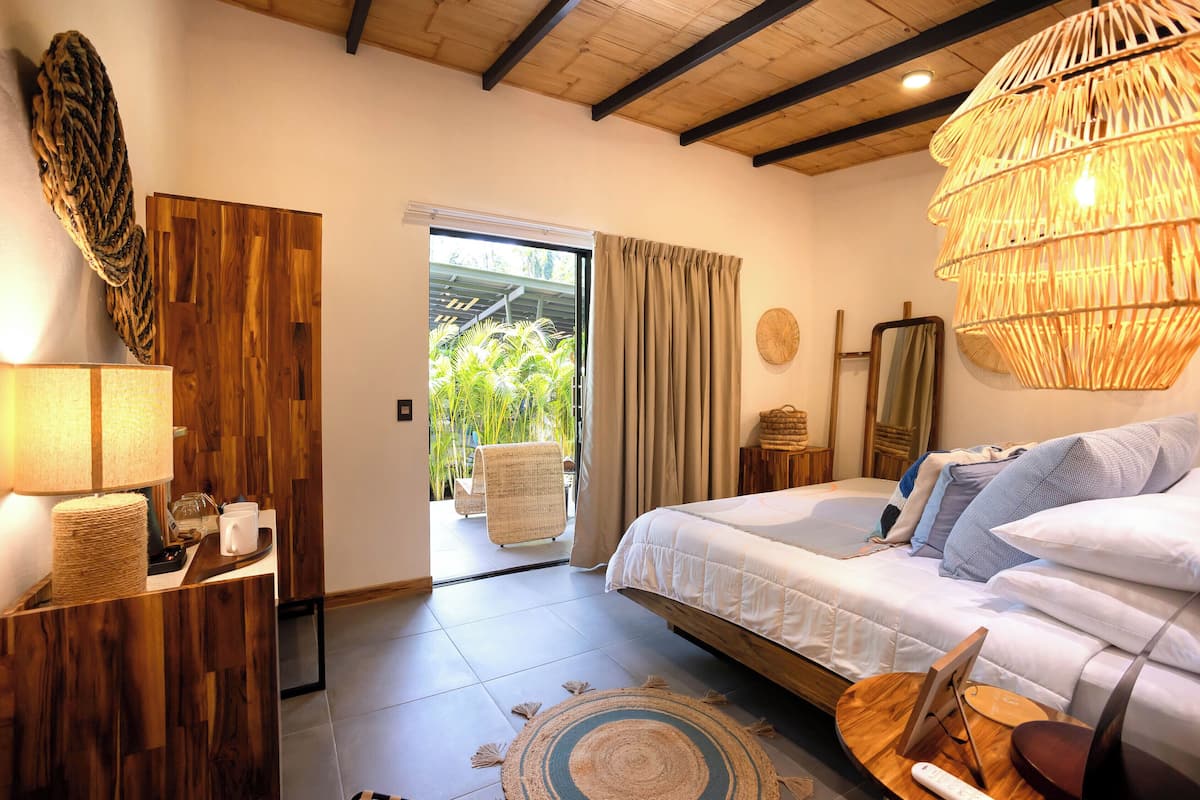 Un dormitorio con cama, mesita de noche, lámpara y vistas al exterior.