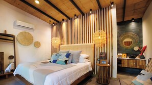 A modern bedroom with a large bed, a wooden ceiling, a wall-mounted air conditioner, and a decorative mirror. - Exōtico Beach Hotel (Cahuita)