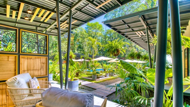 A covered outdoor seating area with wicker chairs and a table, surrounded by lush greenery and a view of the garden. - Exōtico Beach Hotel (Cahuita)