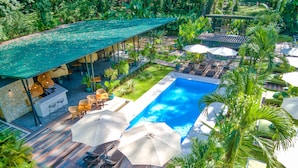 An aerial view of a resort with a swimming pool, lounge chairs, umbrellas, and lush greenery. - Exōtico Beach Hotel (Cahuita)