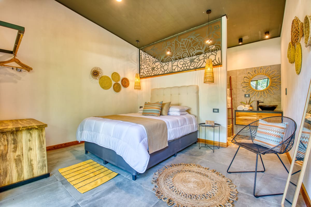 Un dormitorio con cama, mesitas de noche, una silla, cómoda de madera y decoración en la pared.